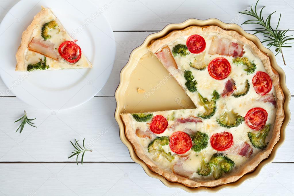 Sliced quiche lorraine traditional homemade french tart pie preparation recipe with tomatoes bacon cheese and broccoli on white vintage table background.
