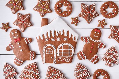 Gingerbreand cookies christmas composition, house man and woman couple, stars, fur trees on white wooden table background. New year traditional dessert food. Top view.