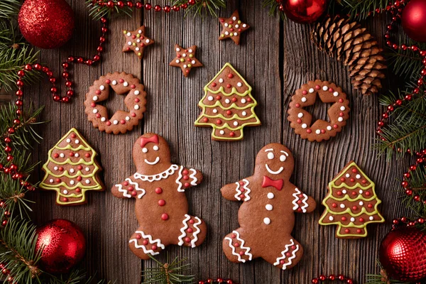 Gingerbread man and woman couple christmas cookies composition in xmas tree decorations frame on vintage wooden table background. Traditional homemade preparation recipe. — Zdjęcie stockowe