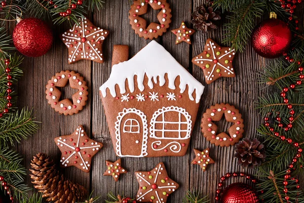 Gingerbread house and stars cookies christmas composition in new year tree decorations on vintage wooden table background. Traditional homemade dessert recipe. Top view. — Stock Fotó