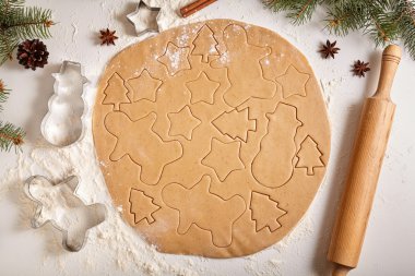 Gingerbread cookies dough preparation recipe with man shape, fir trees, snowman and star forms, cinnamon rolling pin, flour on white kitchen table. Traditional homemade christmas dessert.