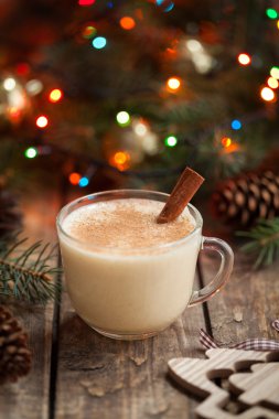 Eggnog traditional christmas holiday egg, vanilla, rum alcohol liqueur drink preparation recipe in two glass cups with cinnamon sticks on wooden vintage table. Colorful bokeh background. shallow depth