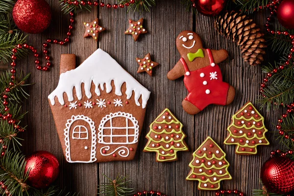 Gingerbread house, man, stars and fir trees cookies christmas composition in new year decorations frame on vintage wooden table background. Homemade traditional dessert recipe. Top view. — 图库照片