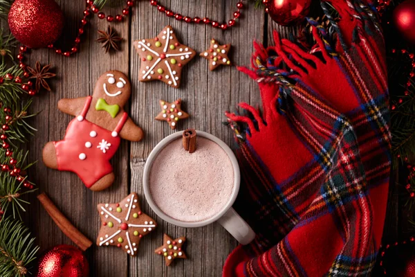 Copa de chocolate caliente con hombre de jengibre, galletas de estrellas y composición de bufanda caliente en marco de decoraciones de abeto sobre fondo de mesa de madera vintage. Receta casera de postre tradicional . — Foto de Stock