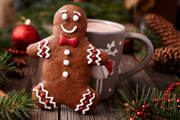 Cup of hot chocolate or cocoa beverage with cinnamon and gingerbread man cookie in new year tree decorations frame on vintage wooden table background. Homemade traditional celebration dessert recipe. — Stock fotografie