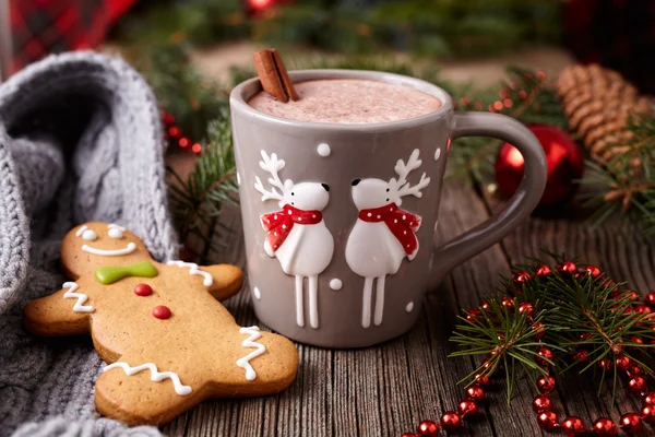 Tasse heißer Schokolade oder Kakaogetränk mit zwei niedlichen Hirschen, Zimt und Lebkuchen-Mann-Weihnachtsplätzchen in Neujahrsbaumschmuck rahmen den Vintage-Holztischhintergrund ein. hausgemachte traditionelle — Stockfoto