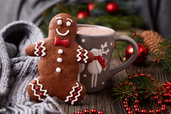 Hot chocolate or cocoa beverage in cup with cute deer, cinnamon and gingerbread man cookie inside new year tree decorations frame on vintage wooden table background. Homemade traditional celebration — Stockfoto