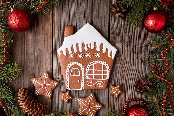 Gingerbread house with stars cookies composition in fir tree decorations frame on vintage wooden table background. Homemade traditional dessert recipe. Top view. — Stock Fotó