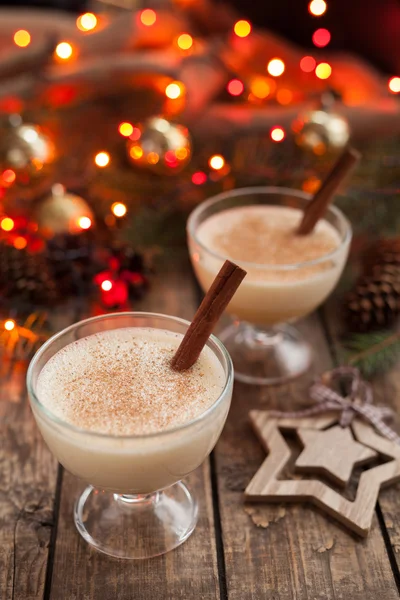 Eggnog traditional xmas homemade winter egg, vanilla non alcohol liqueur preparation recipe in two glass cups with cinnamon sticks on wooden vintage table. Red bokeh background. shallow depth of field