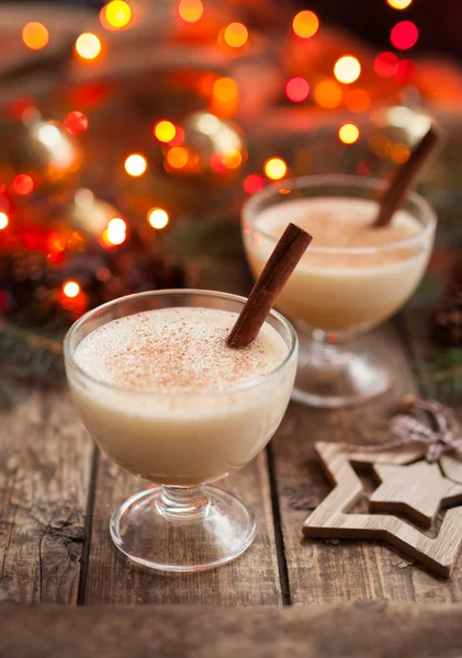 Ovo de Natal tradicional de gemada, receita de preparação de licor de baunilha sem álcool em duas xícaras de vidro com paus de canela na mesa vintage de madeira. Fundo bokeh vermelho. profundidade de campo rasa — Fotografia de Stock