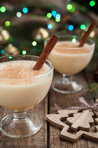 Huevo tradicional de Navidad huevo, licor de ron de vainilla preparación de licor receta en dos tazas de vidrio con palitos de canela en la mesa vintage de madera. Fondo bokeh azul y verde. profundidad de campo poco profunda —  Fotos de Stock