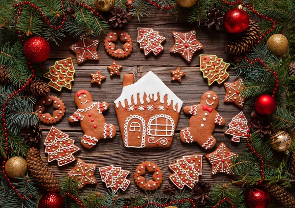 Gingerbread man and woman couple, house, fir trees, stars cookies composition in christmas decorations frame on vintage wooden table background.