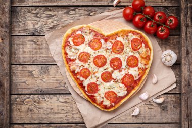 Heart shaped pizza margherita with tomatoes, mozzarella and garlic on vintage wooden table background. Symbol of vegetarian romantic love.