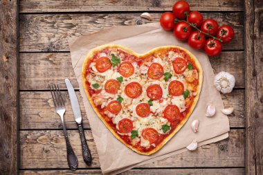 Vegetarian heart shaped pizza margherita with tomatoes, mozzarella, parsley and garlic on vintage wooden table background. Food concept of romantic love.