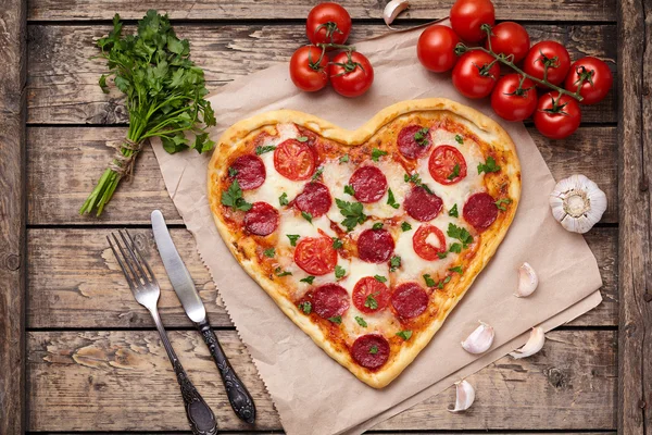 Pizza em forma de coração para o dia dos namorados com pepperoni, mussarela, tomate, salsa e alho no fundo da mesa de madeira vintage. Símbolo de comida de amor romântico . — Fotografia de Stock