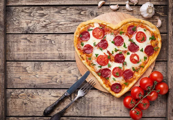 Herzförmige Pizza mit Peperoni, Tomaten und Mozzarella auf altem Holztischhintergrund. Valentinstag Liebe Konzept. — Stockfoto