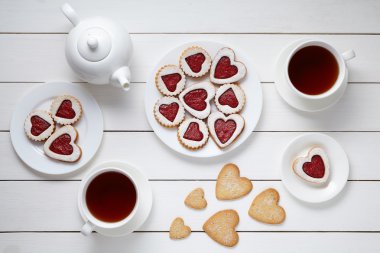 Heart shaped cookies for Valentines day with teapot and two cups of tea on white wooden background.