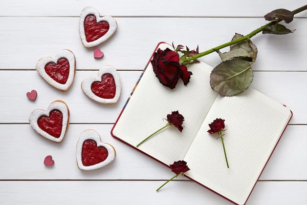 Herzförmige Plätzchen mit leerem Notizbuch und Rosen auf weißem Holzhintergrund zum Valentinstag. — Stockfoto