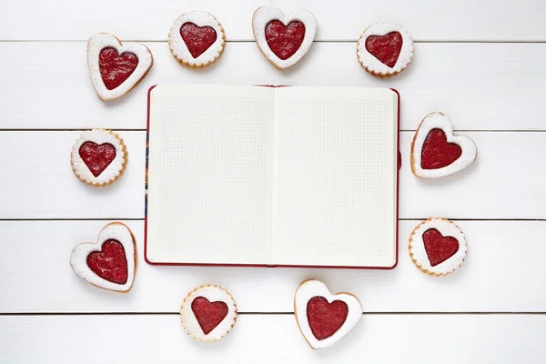 Empty notebook frame for design text and heart shaped cookies on white wooden background. — Stok fotoğraf