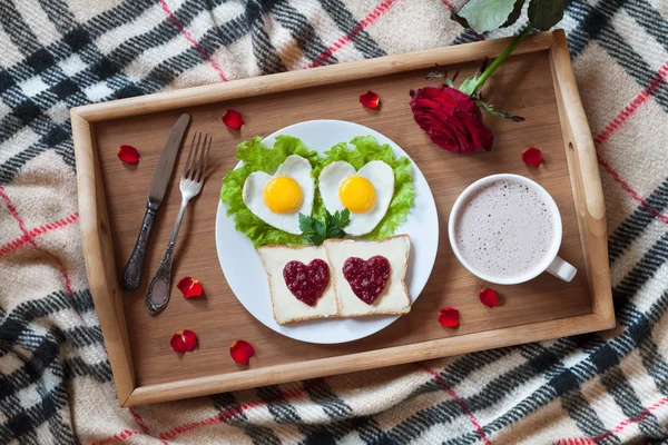 Breakfast in bed with heart-shaped eggs, toasts, jam, coffee, rose and petals. Valentines Day surprise. — Zdjęcie stockowe