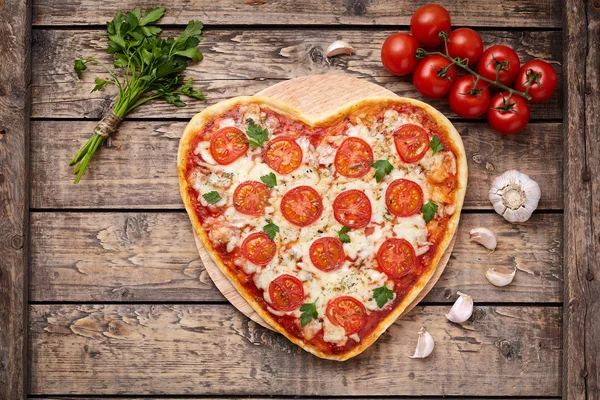 Heart shaped pizza margherita romantic love food concept with mozzarella, tomatoes, parsley, and garlic composition on cutting board, vintage wooden table background. — Zdjęcie stockowe