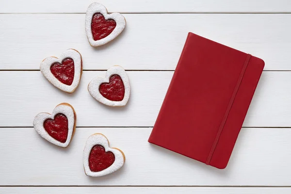 Cookies em forma de coração com caderno vermelho vazio, composição em fundo de madeira branca para o dia dos namorados . — Fotografia de Stock