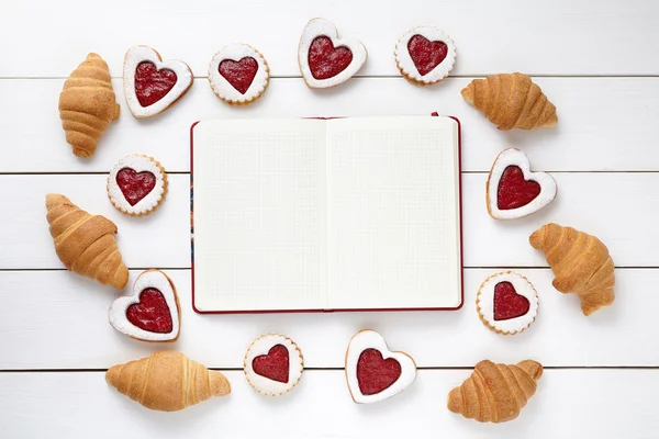 Empty notebook frame for design text, croissants and heart shaped cookies composition on Valentines Day — Zdjęcie stockowe