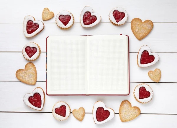 Empty notebook frame for design text and heart shaped cookies on white wooden background.