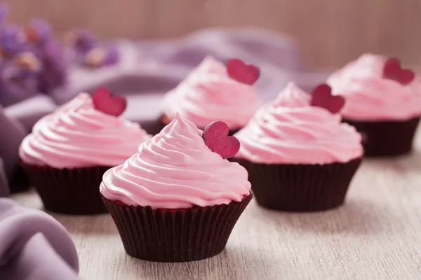 Cupcakes traditionell fest söta dessert med rosa grädde och röda hjärtan på rad på vintage bakgrund — Stockfoto