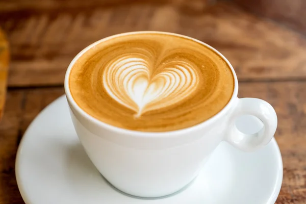 Cerrar taza de café blanco con forma de corazón arte latte en pestaña de madera — Foto de Stock