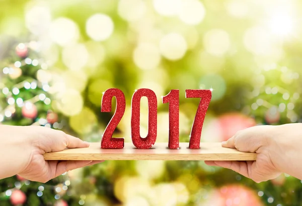 Hand holding wood plate with 2017 new year red glitter number at — Stock Photo, Image