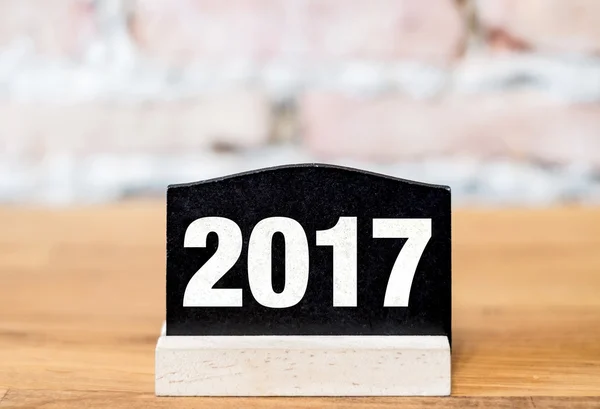 Nuevo año 2017 número en el letrero de pizarra en la mesa de madera en ladrillo w — Foto de Stock