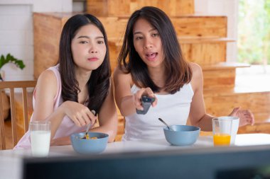 Mutlu Asyalı lezbiyen çift evde kahvaltı yaparken televizyon seyrediyor.
