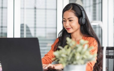 İçerik yaratıcısı olarak Asyalı bir kadın dizüstü bilgisayarda yazarak evden çalışırken podcast dinliyor. Teknoloji kullanılarak yeni normal yaşam tarzı