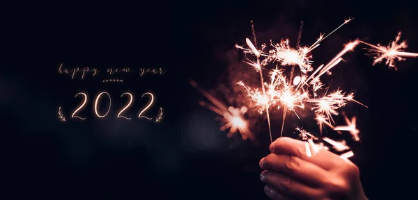 欢庆2022年新年 手拿着燃烧的火焰喷射器 深夜背景为黑色 节日庆祝会 色彩斑斓的色调 — 图库照片