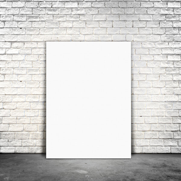 Blank Poster paper standing next to a white brick wall.