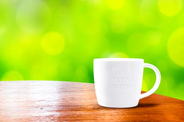 Mesa redonda de madera con taza blanca con fondo bokeh verde — Foto de Stock