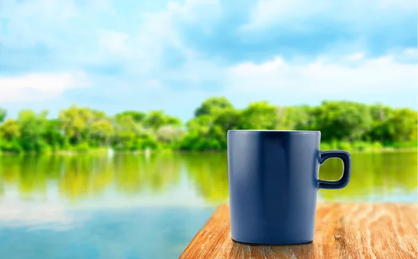 Blue Coffee cup on wood table at blur tree and lagoon background — Stock Photo, Image