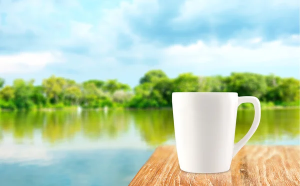 ぼかしのツリーとラグーンの比較で木製テーブルの上の白いコーヒー カップ — ストック写真