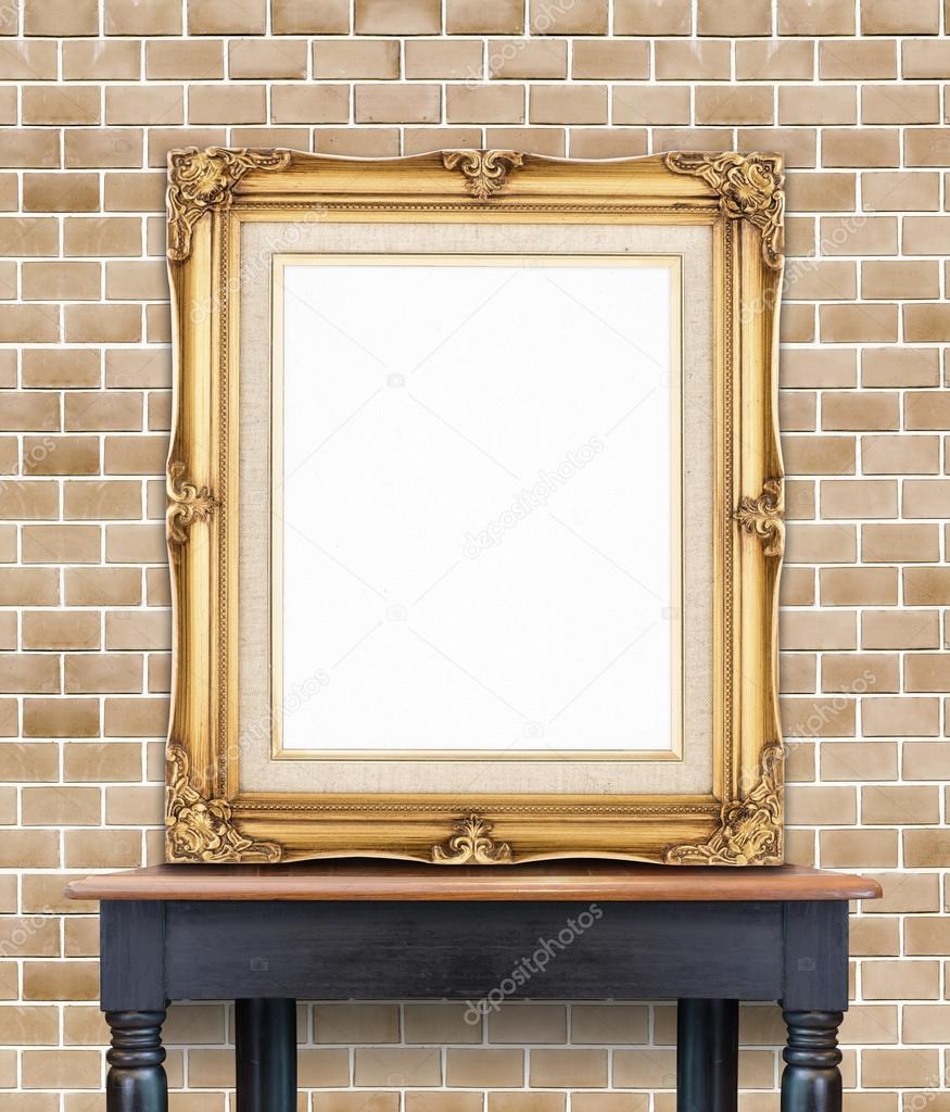 Blank vintage golden photo frame lean at pale orange brick wall on wood table,Template Mockup for add picture.