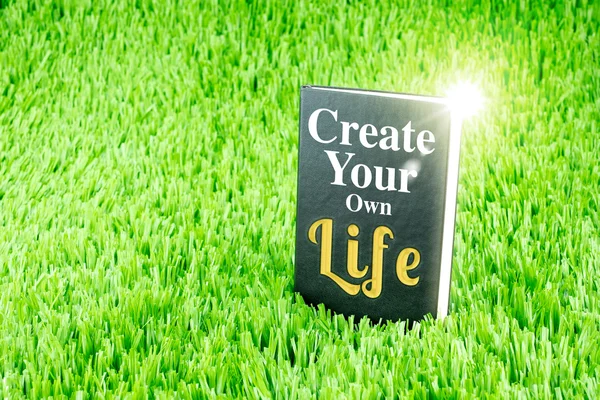 Glänzendes schwarzes Buch auf Gras mit dem Wort "Create your own life", — Stockfoto