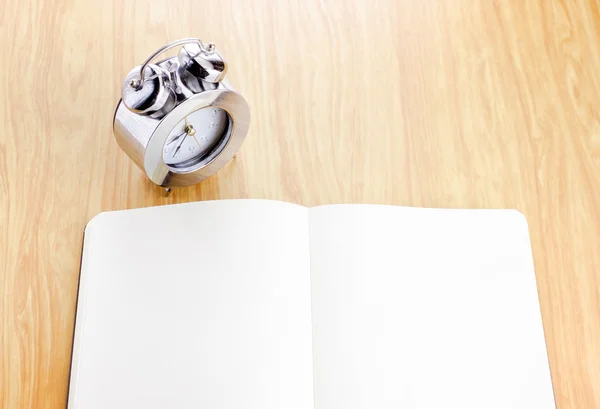 Blank open notebook with silver alarm clock beside it on wooden — Stock Photo, Image