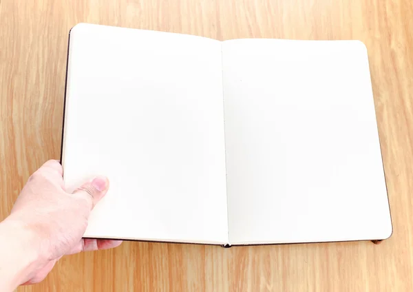 La mano que sostiene el cuaderno abierto en blanco lo puso en la mesa de madera, plantilla —  Fotos de Stock