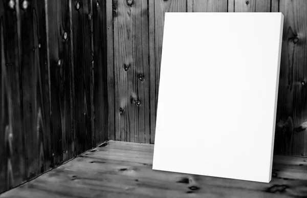 Blank white poster leaning at black and white wooden wall in pla