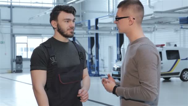 Mechaniker beschäftigt sich mit Kunden über Autoreparatur — Stockvideo