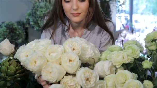 Девушка-флористка смотрит на белые розы в цветочном магазине — стоковое видео