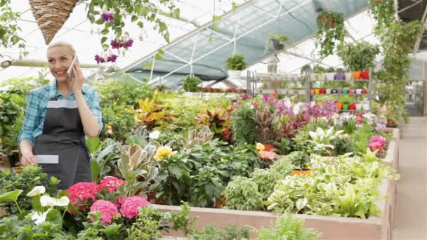 Floristería femenina hablando por teléfono en el centro del jardín — Vídeo de stock