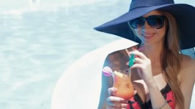 Woman poses with glass of coktail near the swimming pool