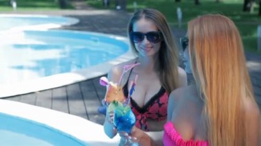 İki kadın havuz kenarında kokteyl içiyor