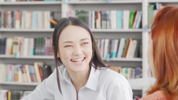 Encantadora joven asiática disfrutando de estudiar con su amigo en la biblioteca — Vídeos de Stock
